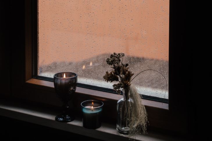 Una finestra al tramonto, fori piove, sul davanzale candele accese creano calore e autenticità